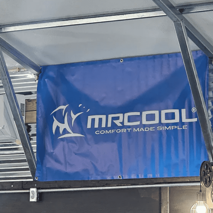Blue and white "mrcool" mini-split air conditioner banner displaying a corporate logo and slogan "comfort made simple," mounted under a metal shelter.