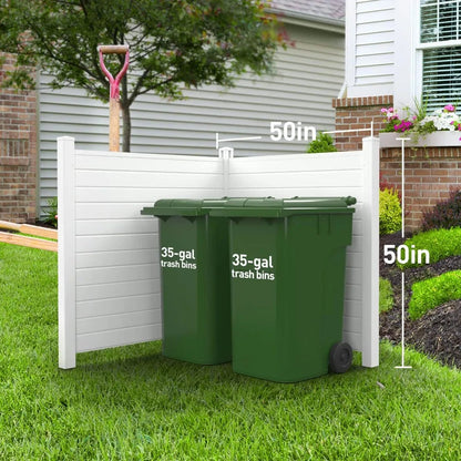 A white, weather-resistant L-shaped privacy panel measuring 50 inches in height encloses two green 35-gallon trash bins placed on a lawn. A pink-handled shovel leans against the Condenser Fence Privacy Shield Fence Panels - Hide Unsightly Outdoor Equipment with Ease. A house with flower boxes is visible in the background.