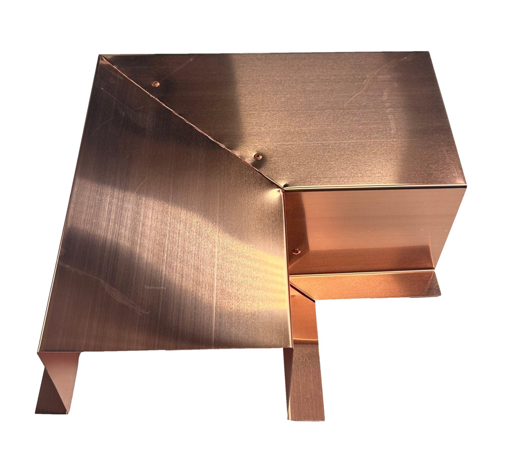 A copper-colored, geometrically designed object with angular shapes and smooth surfaces. It has an elevated base and reflective metallic finish, creating a modern and industrial aesthetic. The design ensures easy installation, complementing the premium quality Perma Cover Residential Series - Line Set Cover Side Turning Elbows - Premium Quality used in HVAC line sets.