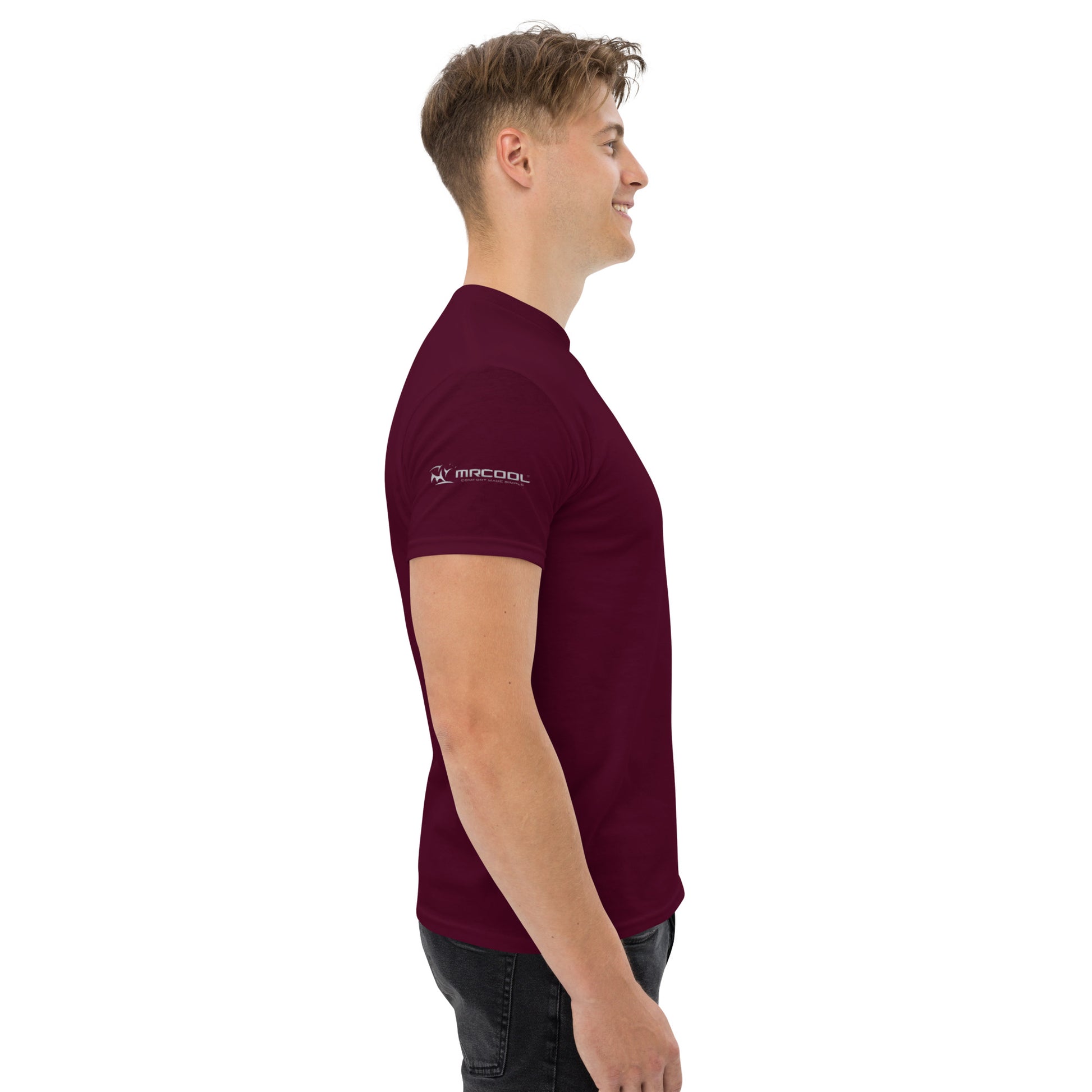 Side view of a smiling young man in a Exclusive HVAC-Themed Custom Tee by MRCOOL DIY Direct, standing against a white background. The t-shirt has a logo on the left chest.