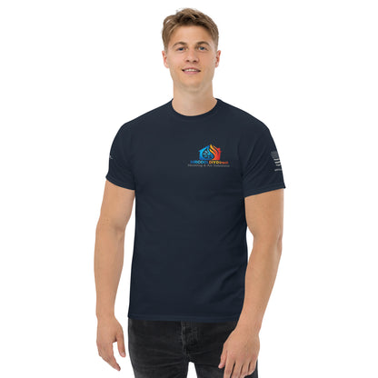 A young man in a dark blue, Exclusive HVAC-Themed Custom Tee by MRCOOL DIY Direct with a colorful logo on the chest and text on the sleeves, standing against a white background, smiling slightly.