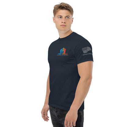 A young man wearing a dark navy, Exclusive HVAC-Themed Custom Tee by MRCOOL DIY Direct with color logos on the chest and a print on the right sleeve, standing against a plain background, looking to his left.